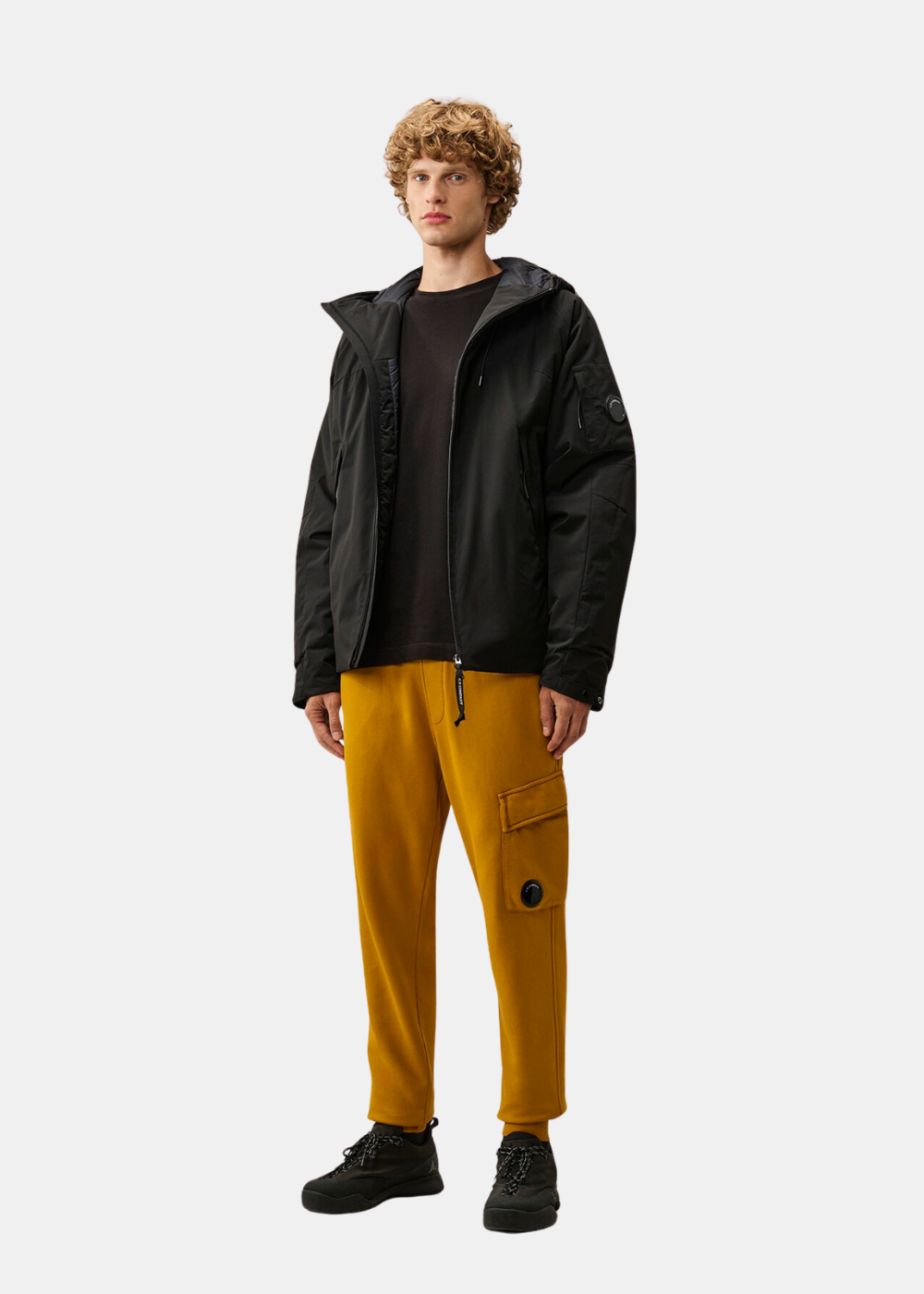 Mannequin homme portant le t-shirt noir C.P. Company sous une veste noire avec pantalon de survêtement jaune
