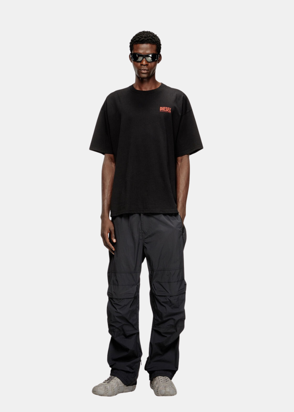 Look complet homme:
t-shirt noir Diesel oversize, overalon pantalon cargo noir baskets grises et lunettes de soleil.