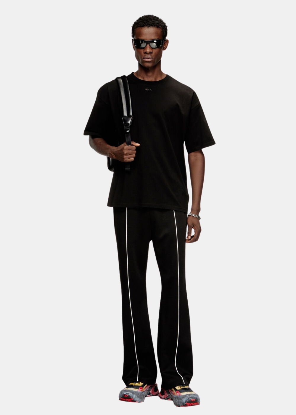 Silhouette complète associant le t-shirt noir Diesel à un pantalon noir à liserés blancs et des lunettes de soleil