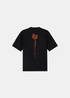 T-shirt noir à manches courtes posé à plat, vue de dos, montrant le logo boussole orange surmontant une inscription verticale de coordonnées.