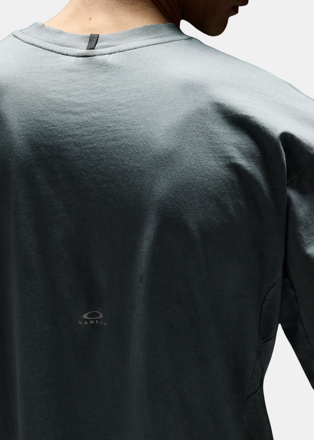 Zoom sur le haut du dos du t-shirt Oakley gris ciment montrant le petit logo réfléchissant et le col.