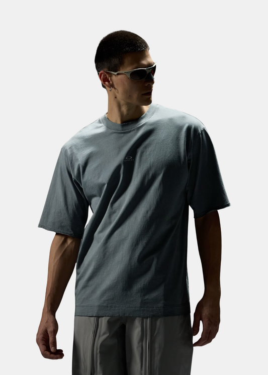 T-shirt Oakley gris ciment à la coupe oversize porté de face avec lunettes de soleil.