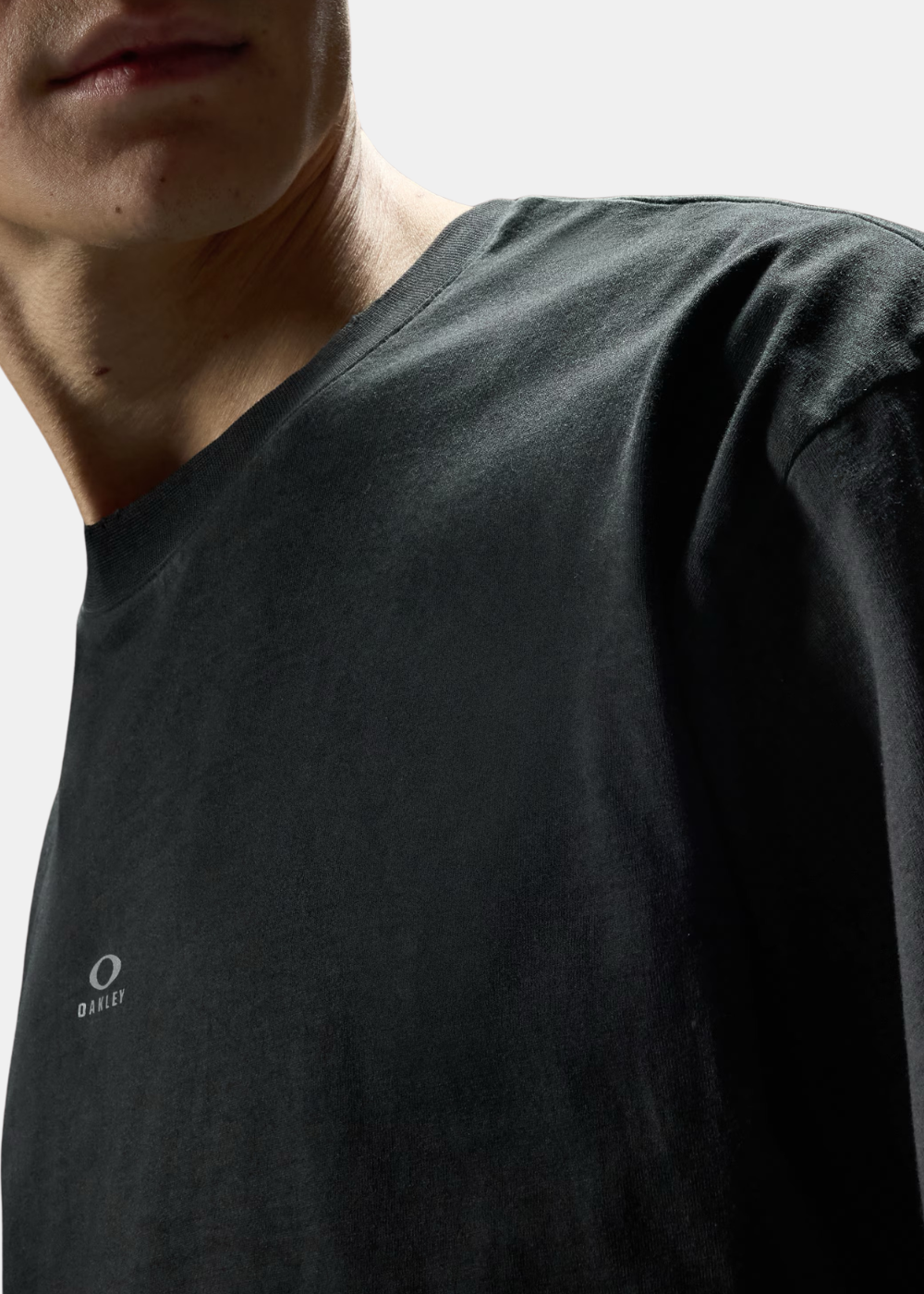 Zoom sur le haut de la poitrine du t-shirt Oakley noir montrant le logo réfléchissant et la patte de col