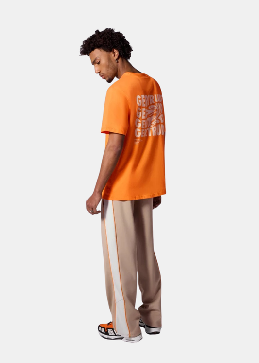 Silhouette de dos avec t-shirt orange Gertrude à imprimé graphique blanc, pantalon beige et baskets