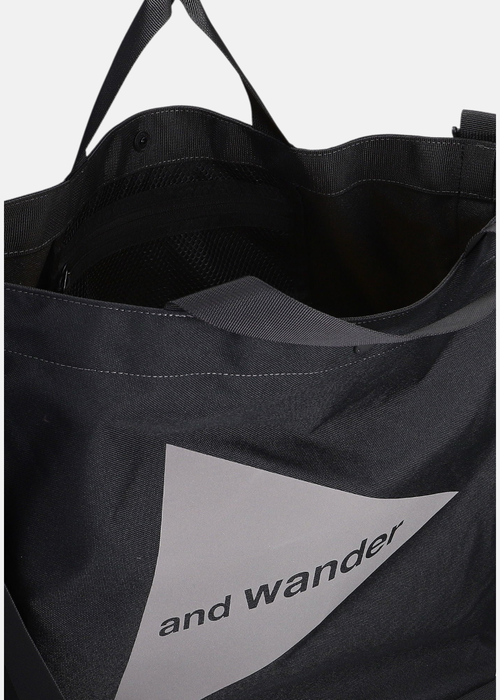 Gros plan sur l'ouverture et l'intérieur du tote bag And Wander noir, montrant le tissu et le logo.