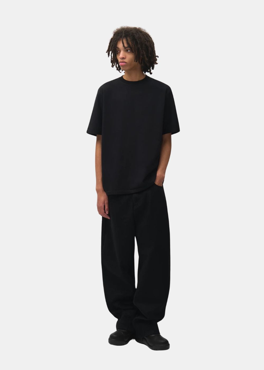 Vue de face du t-shirt Arte Antwerp noir col rond porté avec un pantalon ample noir.