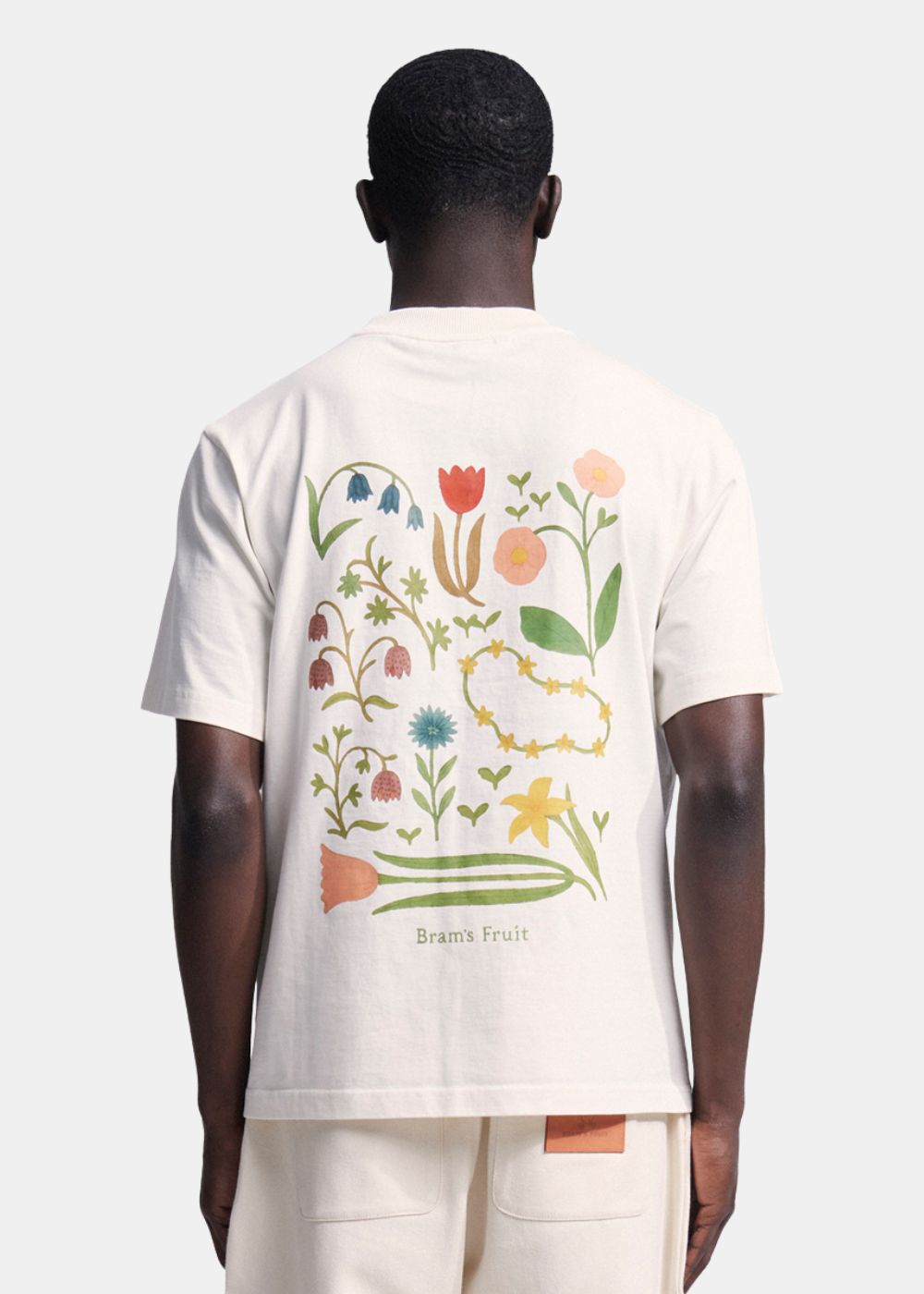 Vue de dos du t-shirt blanc montrant l'imprimé artistique composé de plusieurs fleurs colorées réparties sur le coton lourd.