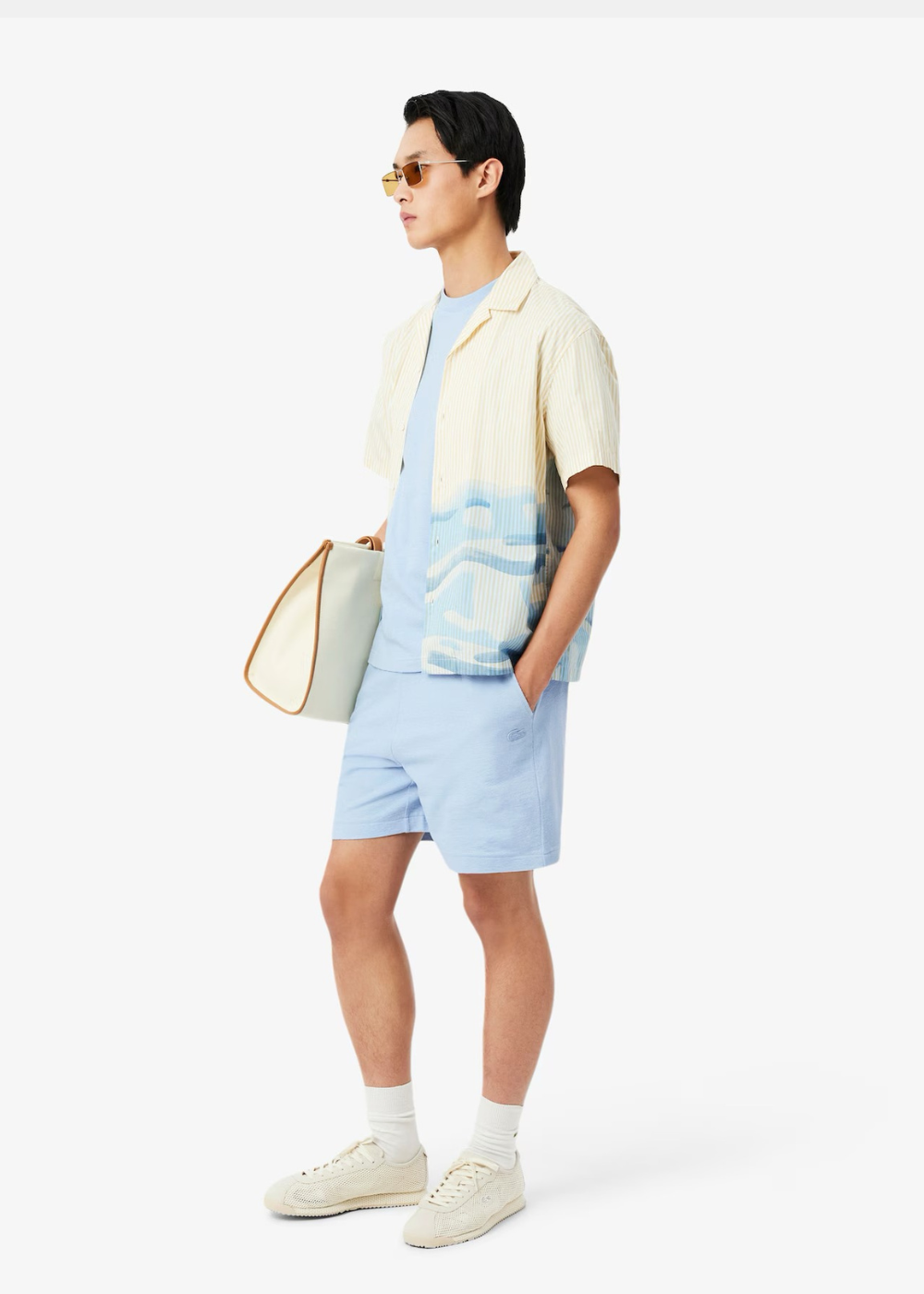 Homme portant un t-shirt bleu ciel Lacoste avec une chemisette ouverte et un short assorti, vue de profil.