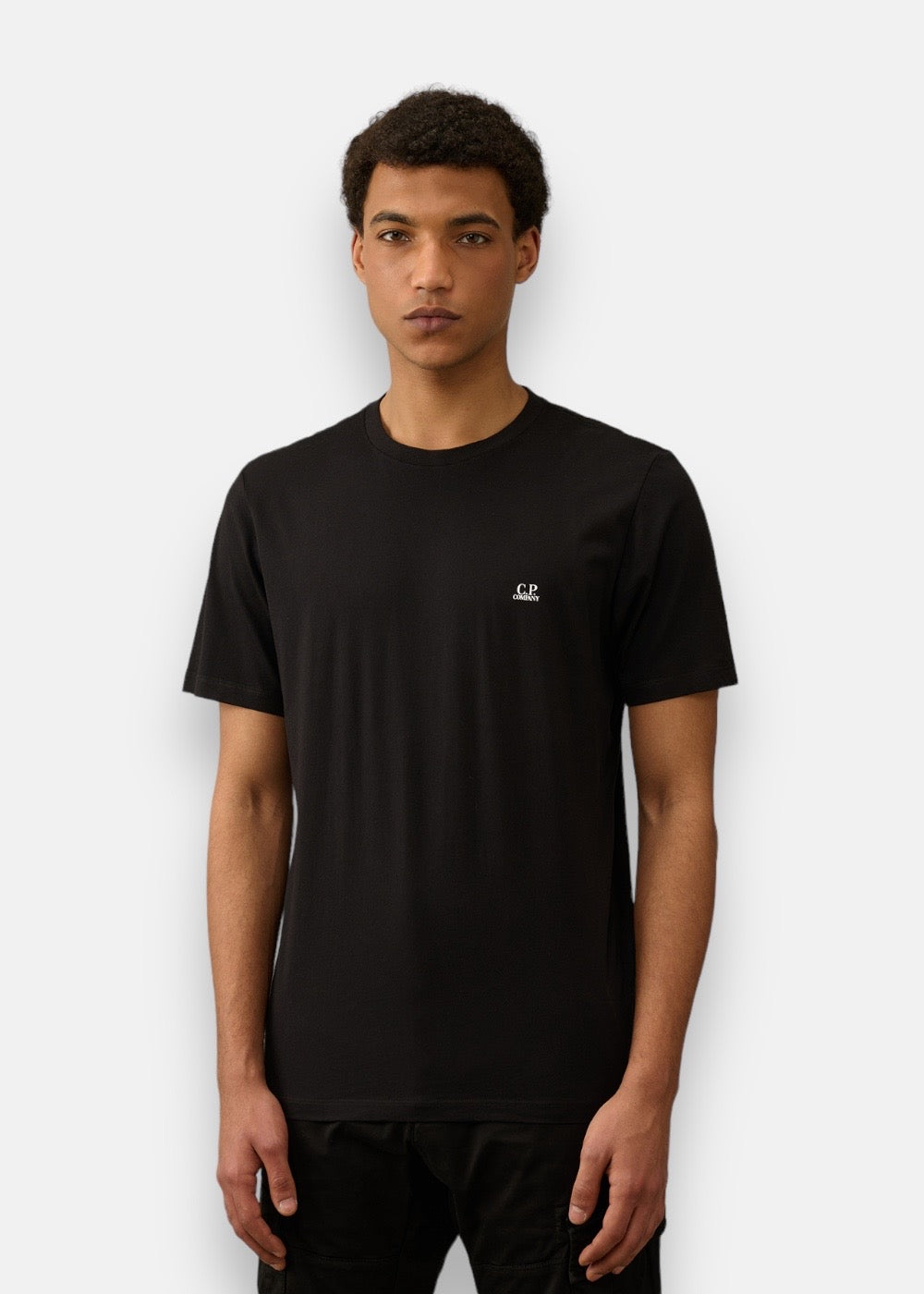 Homme portant le T-shirt C.P. Company noir, petit logo sur la poitrine.