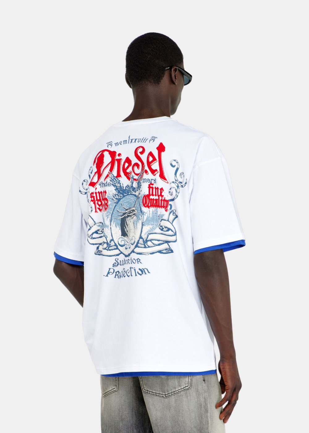 Vue de dos du t-shirt Diesel blanc porté par un mannequin, révélant un grand graphique héraldique imprimé composé d'un blason bleu vintage surmonté du logo Diesel en lettres gothiques rouges et des mentions « Superior Protection »