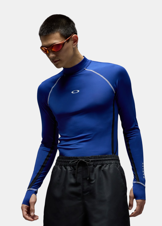 T-shirt de compression bleu à manches longues Oakley avec coutures contrastées blanches, porté de face par un mannequin.