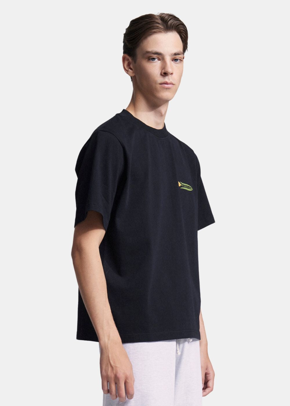Vue de face en 3/4 du mannequin portant le t-shirt noir Bram's Fruit avec un pantalon blanc, coupe décontractée.
