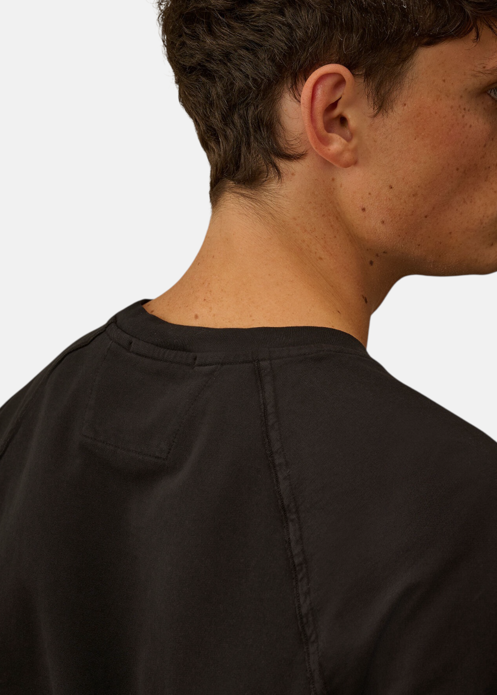 Gros plan sur le col rond côtelé et la couture raglan du t-shirt noir C.P. Company.