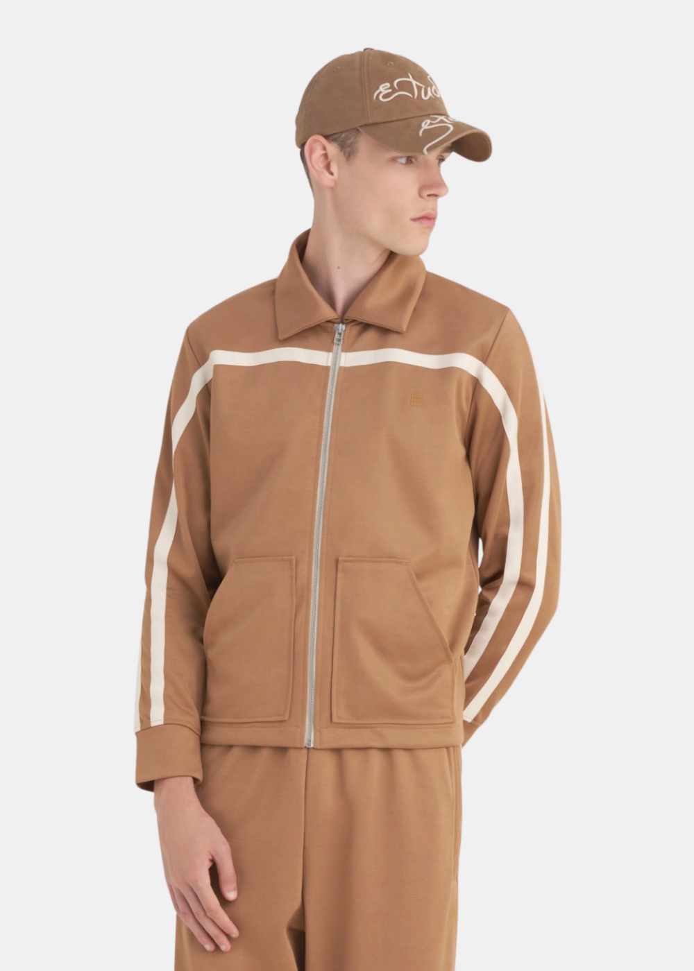 Homme portant la veste de survêtement Études Studio marron, vue de face, coupe droite avec bandes sur les manches.