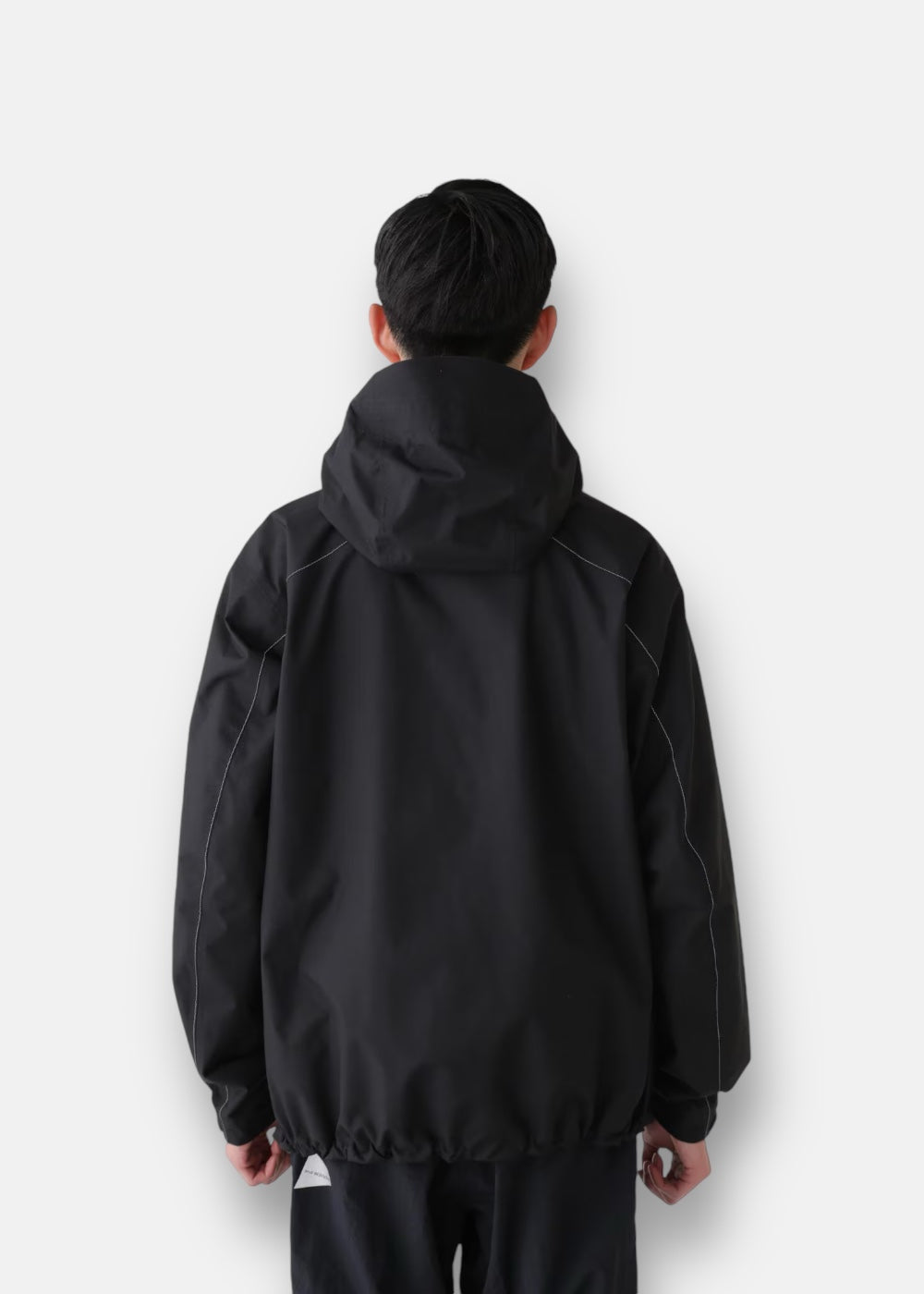 Homme de dos portant la veste And Wander Hiker Rain, mettant en avant la protection thermique et l'imperméabilité.