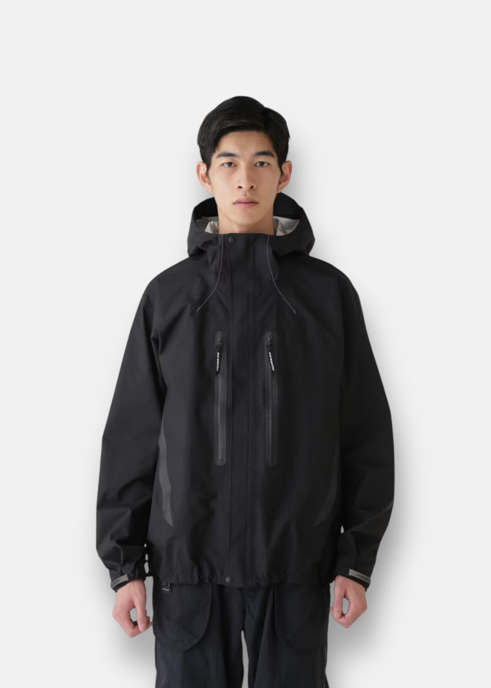 Homme portant la veste technique And Wander Hiker Rain noire, coupe ergonomique pour la randonnée.