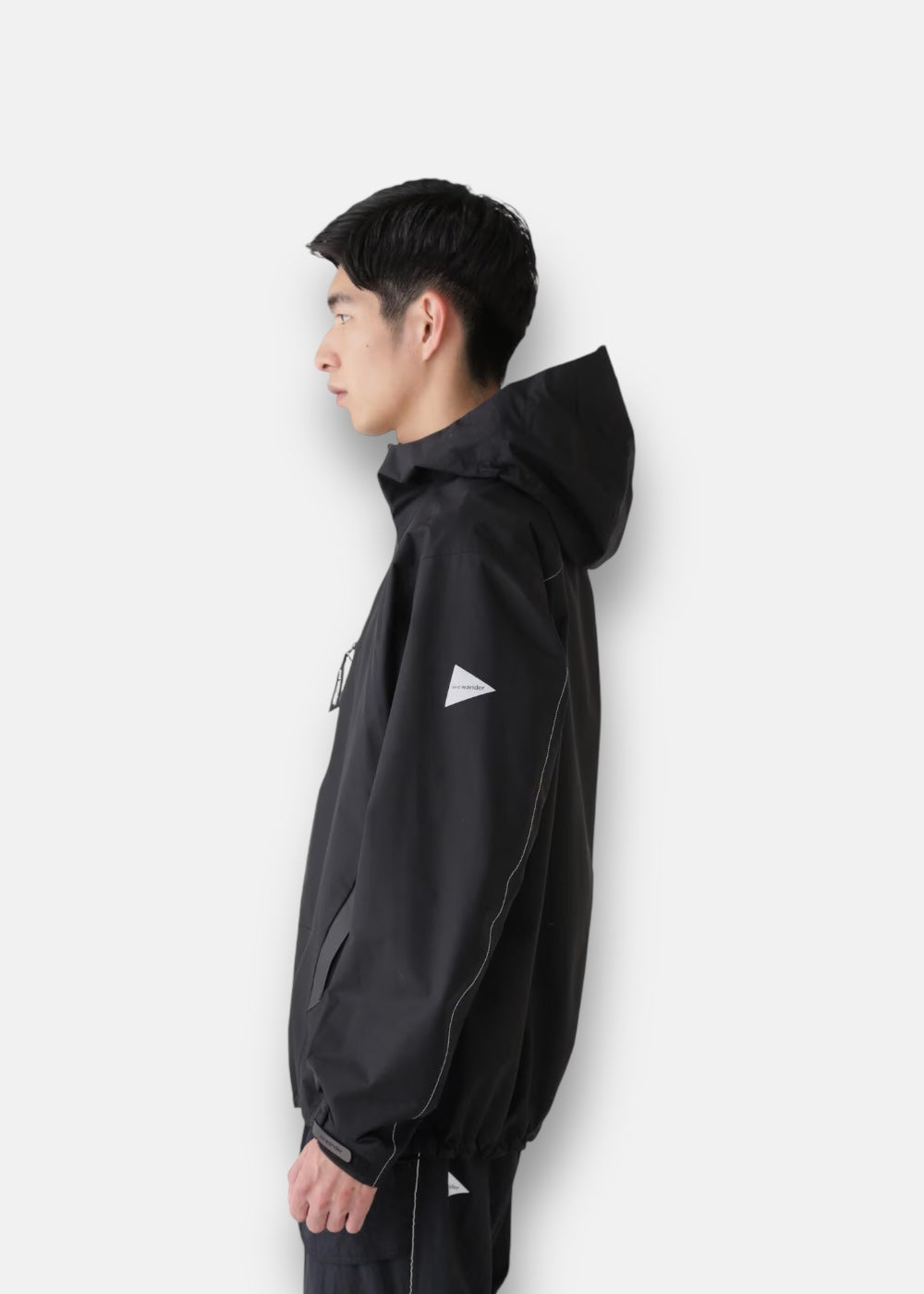 Vue de profil de la veste de pluie And Wander noire portée, montrant l'ajustement des manches et de la capuche.
