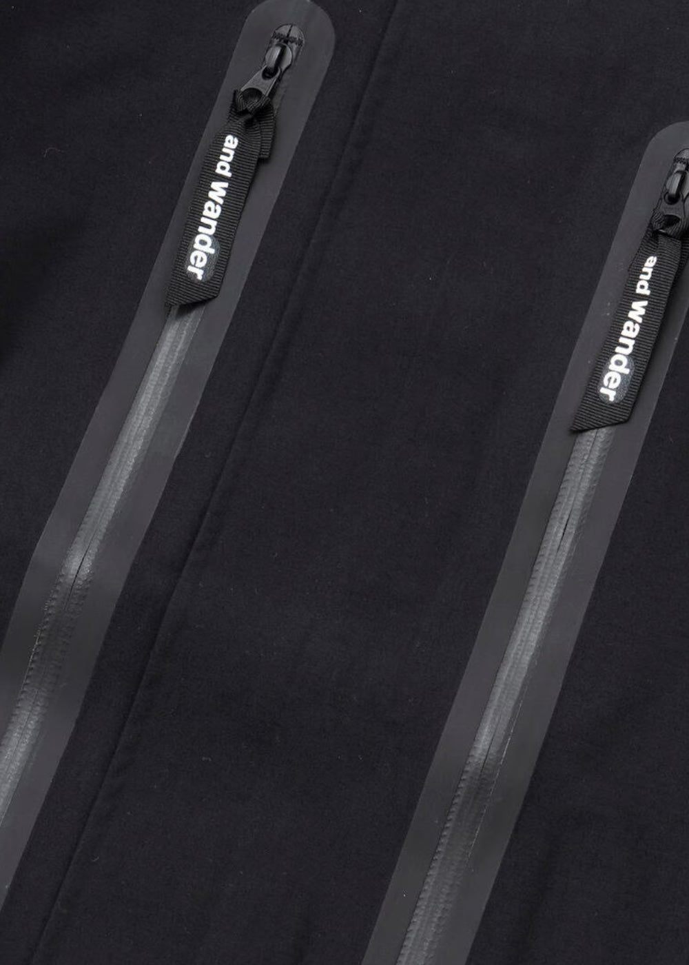 Gros plan sur la poche poitrine zippée avec le logo And Wander réfléchissant.