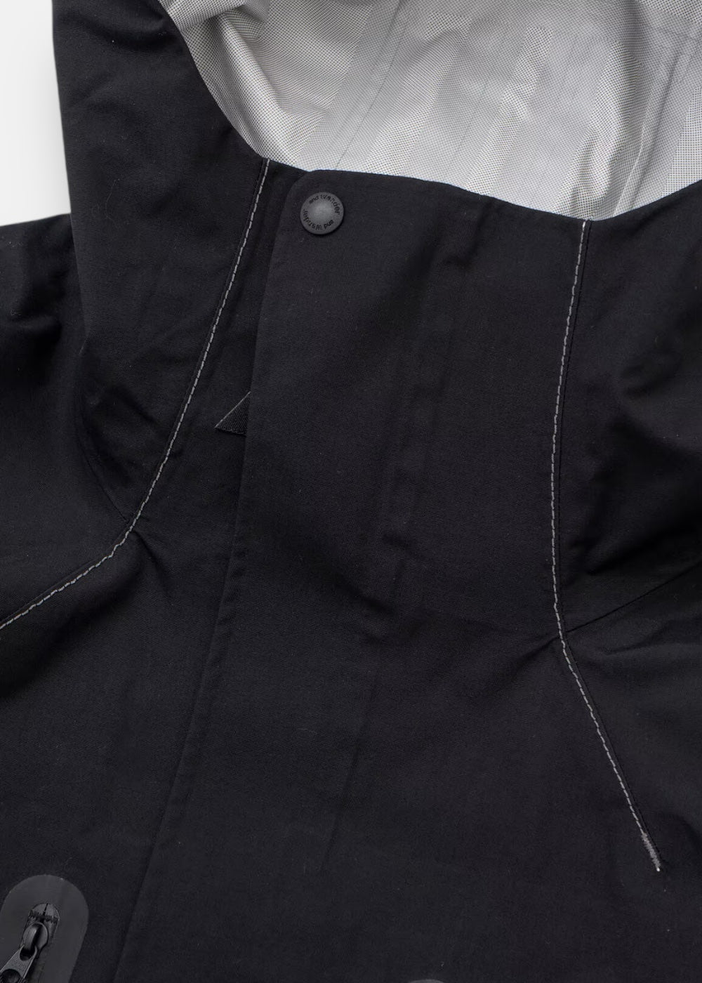 Gros plan sur le rabat de protection par-dessus la fermeture éclair de la veste And Wander, assurant l'étanchéité.