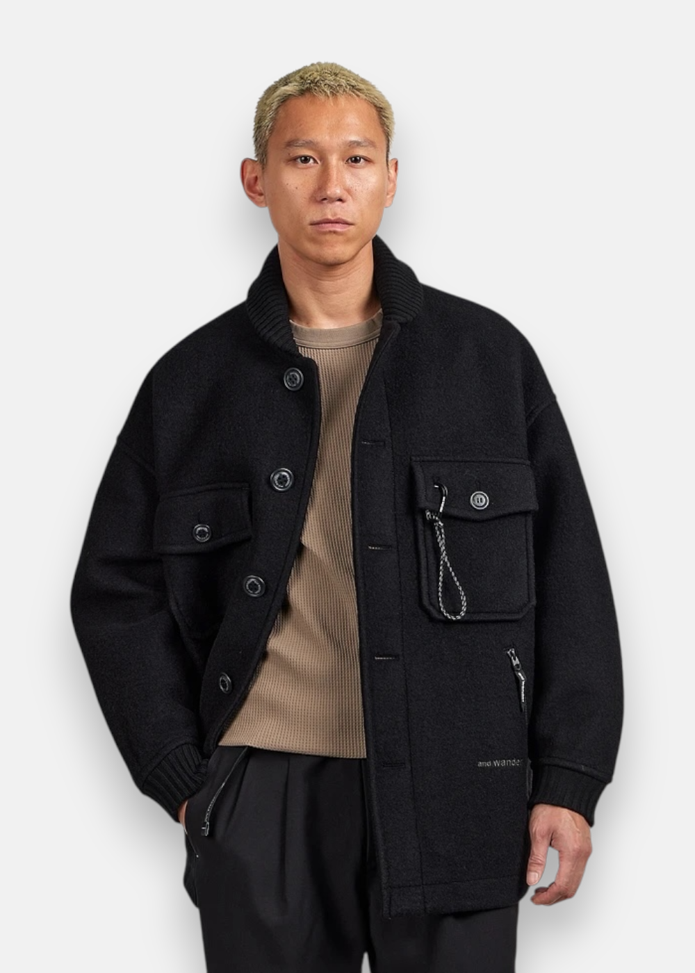 Homme portant la veste And Wander en laine noire, coupe décontractée, look technique.