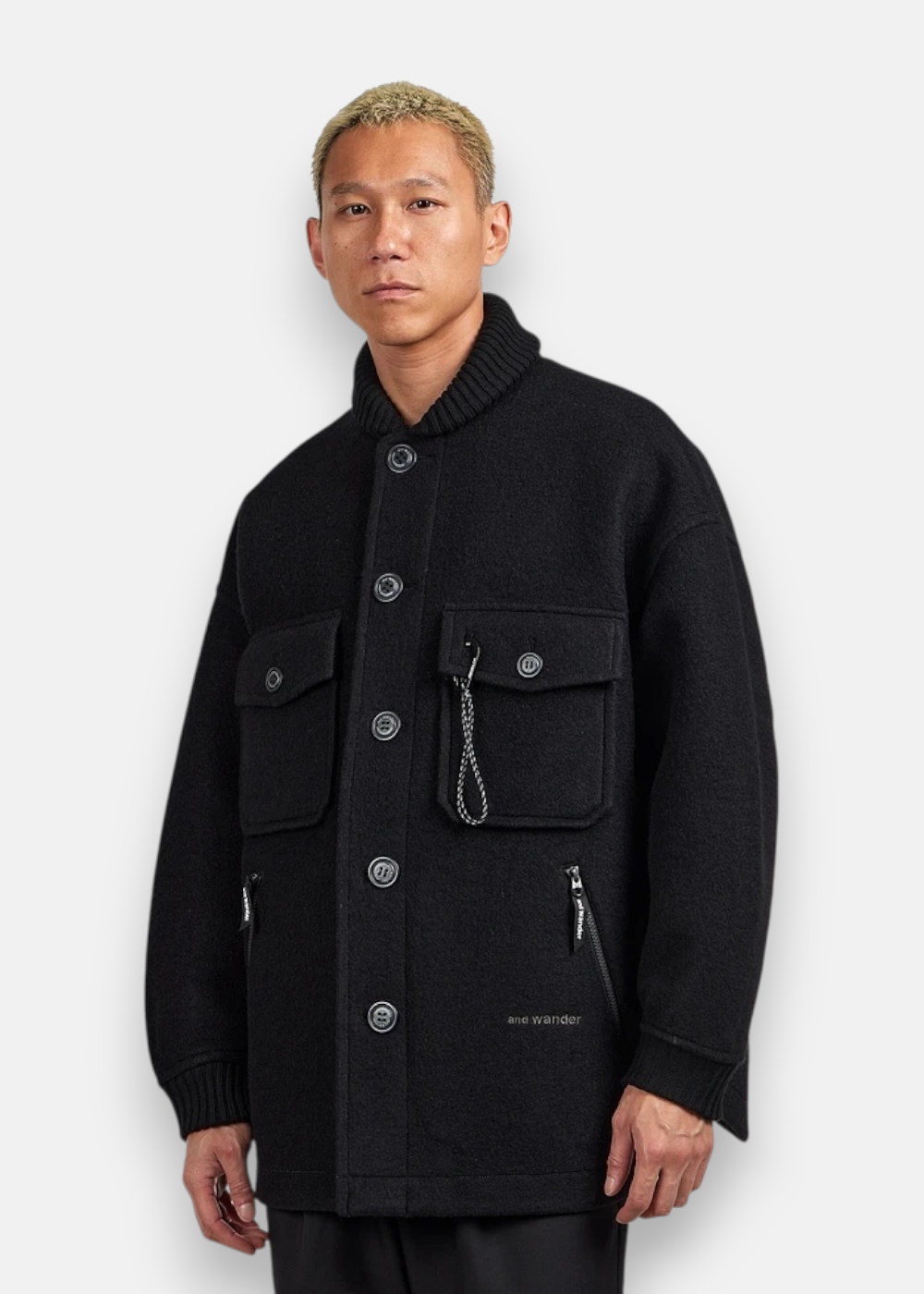 Homme portant la veste And Wander en laine noire, coupe décontractée, look technique.