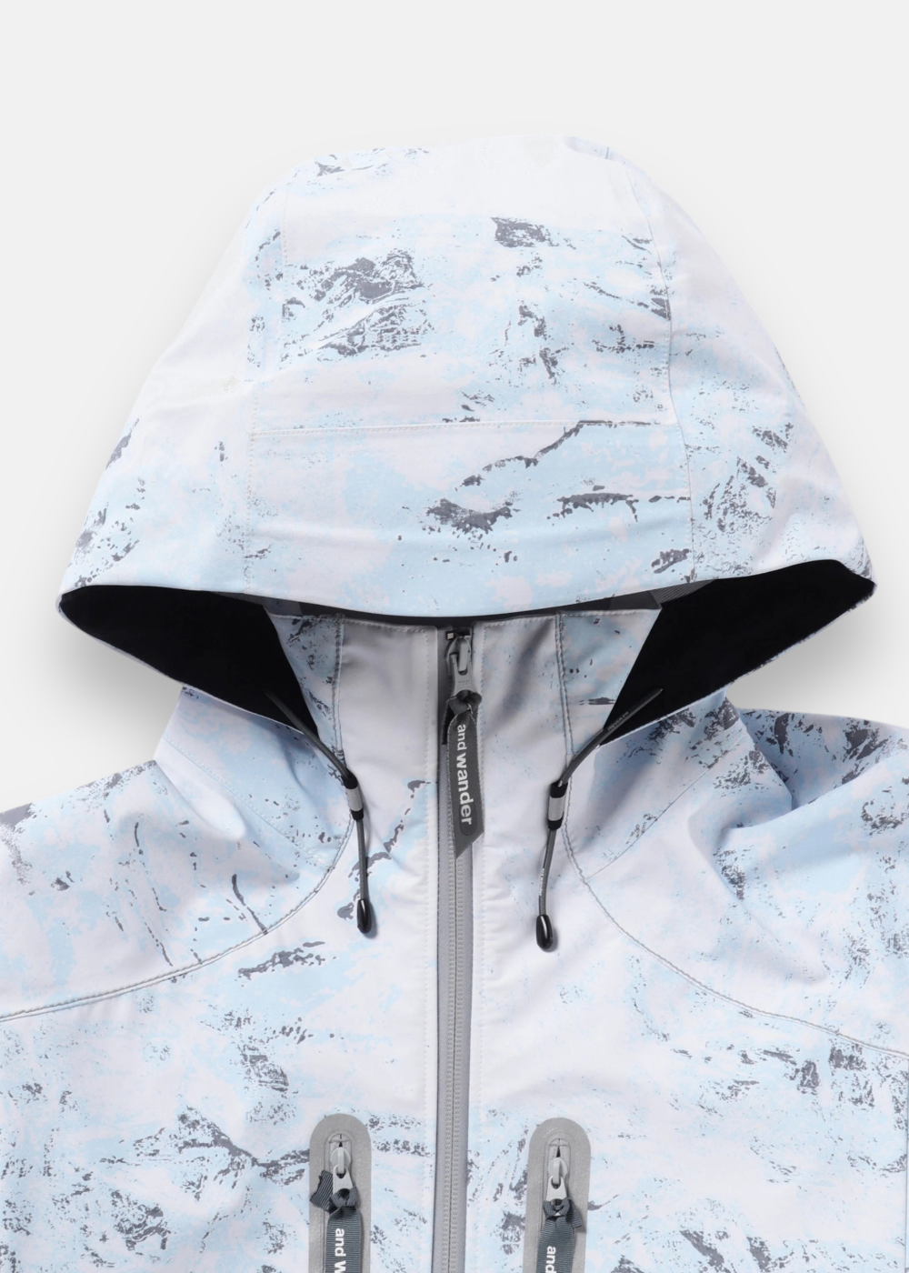 Gros plan sur la capuche, la fermeture éclair et les cordons de serrage de la veste And Wander imprimée PERTEX SHIELD.