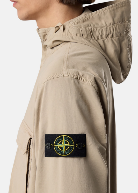 Zoom sur le badge Stone Island sur la manche d'une veste beige avec focus sur la capuche et le profil du mannequin