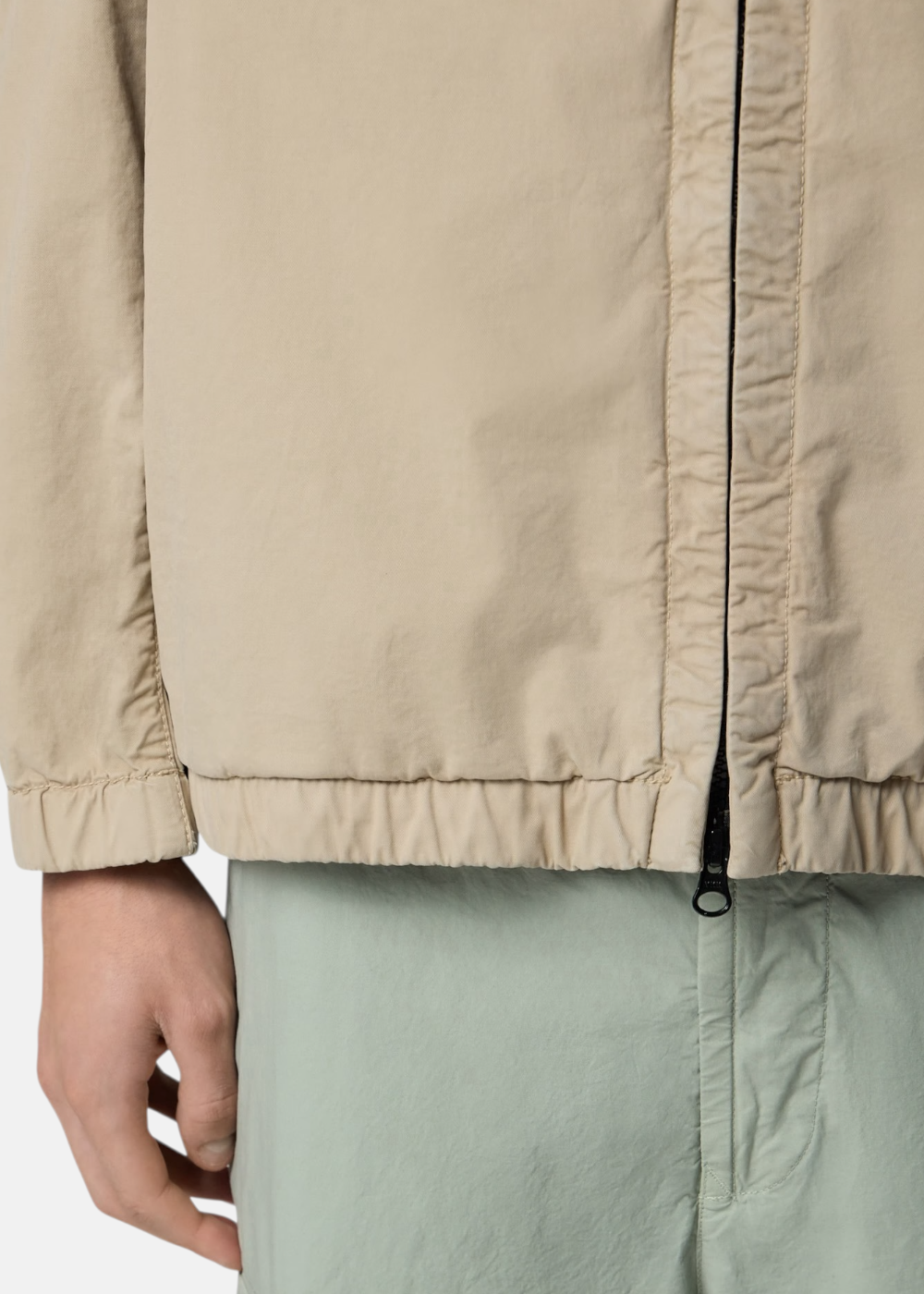 Gros plan sur la glissière bidirectionnelle noire et le bas élastiqué d'une veste à capuche beige Stone Island