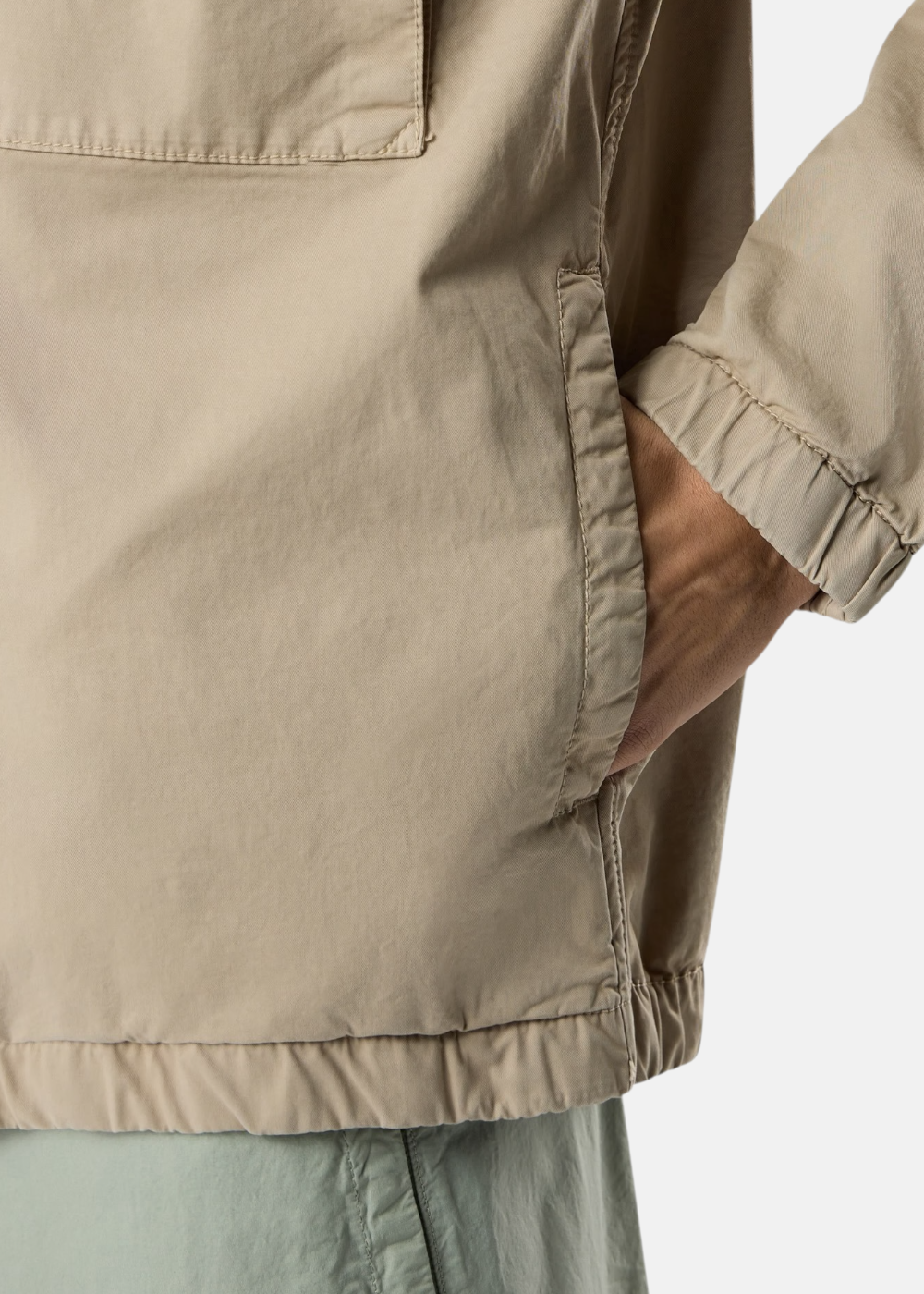 Gros plan sur une poche latérale et la main d'un mannequin insérée dans une veste Stone Island beige