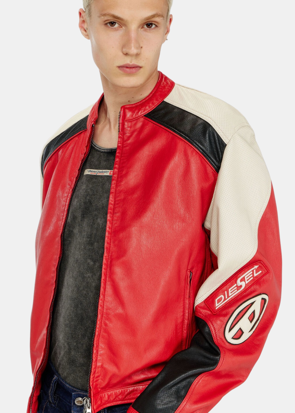 Gros plan de trois-quarts face sur un mannequin portant la veste biker Diesel en cuir rouge, révélant la texture micro-perforée des empiècements blanc cassé et le patch logo ovale embossé sur la manche gauche