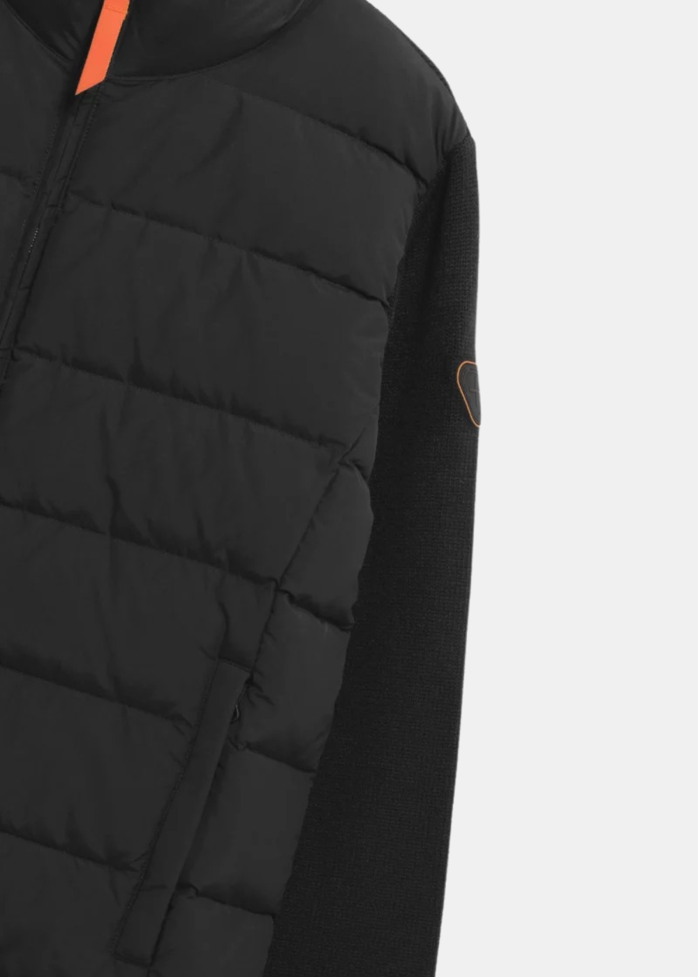 Gros plan sur le matelassage horizontal du buste, la manche en maille avec patch logo Gertrude et la tirette orange sur le zip central
