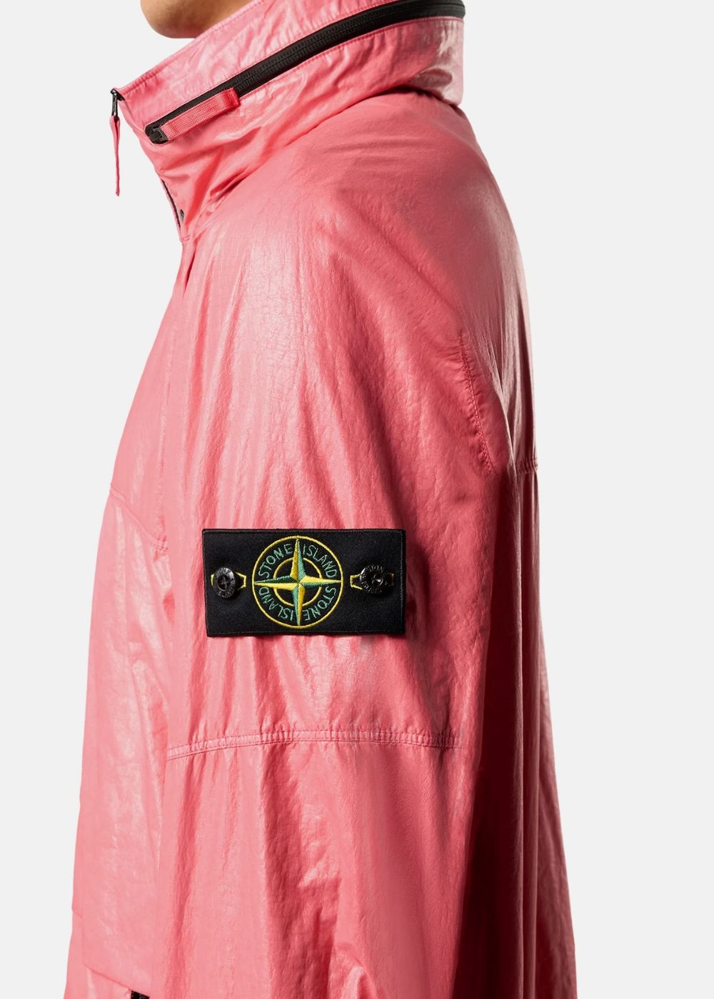 Porté de profil montrant le col montant et le badge boussole Stone Island boutonné sur la manche d'une veste légère rose.