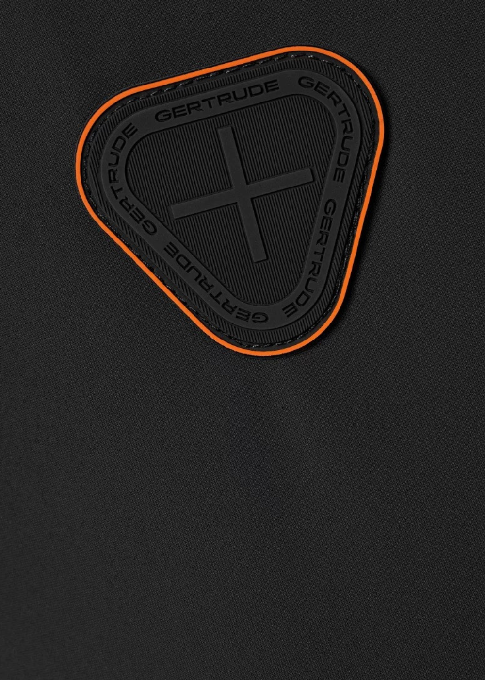 Gros plan sur l'écusson en silicone noir bordé d'orange de la marque Gertrude sur la manche