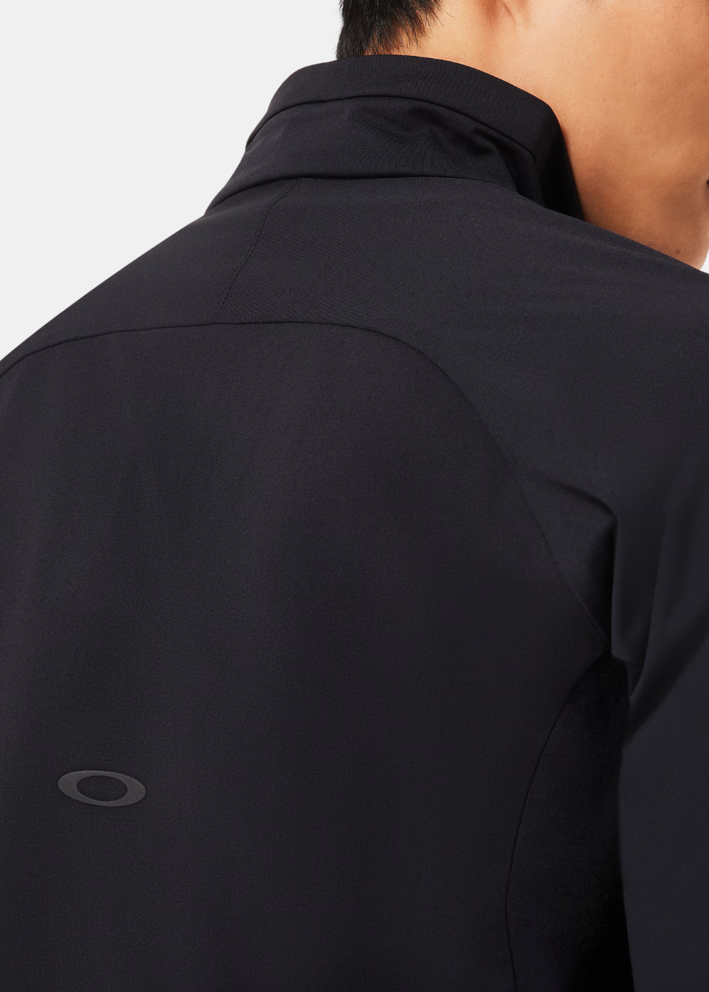 Zoom sur le haut du dos d'une veste de training noire laissant apparaître un petit logo ellipse discret ton sur ton.