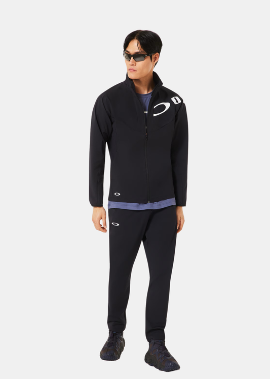 Ensemble de sport avec veste de training noire Oakley, pantalon assorti et lunettes de soleil, porté de face.