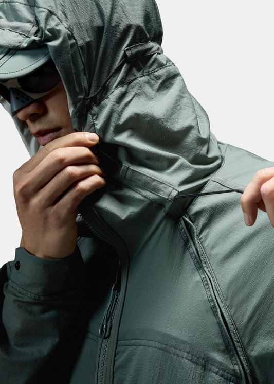 Gros plan sur le réglage de la capuche technique de la veste Oakley verte, portée par-dessus la casquette assortie.