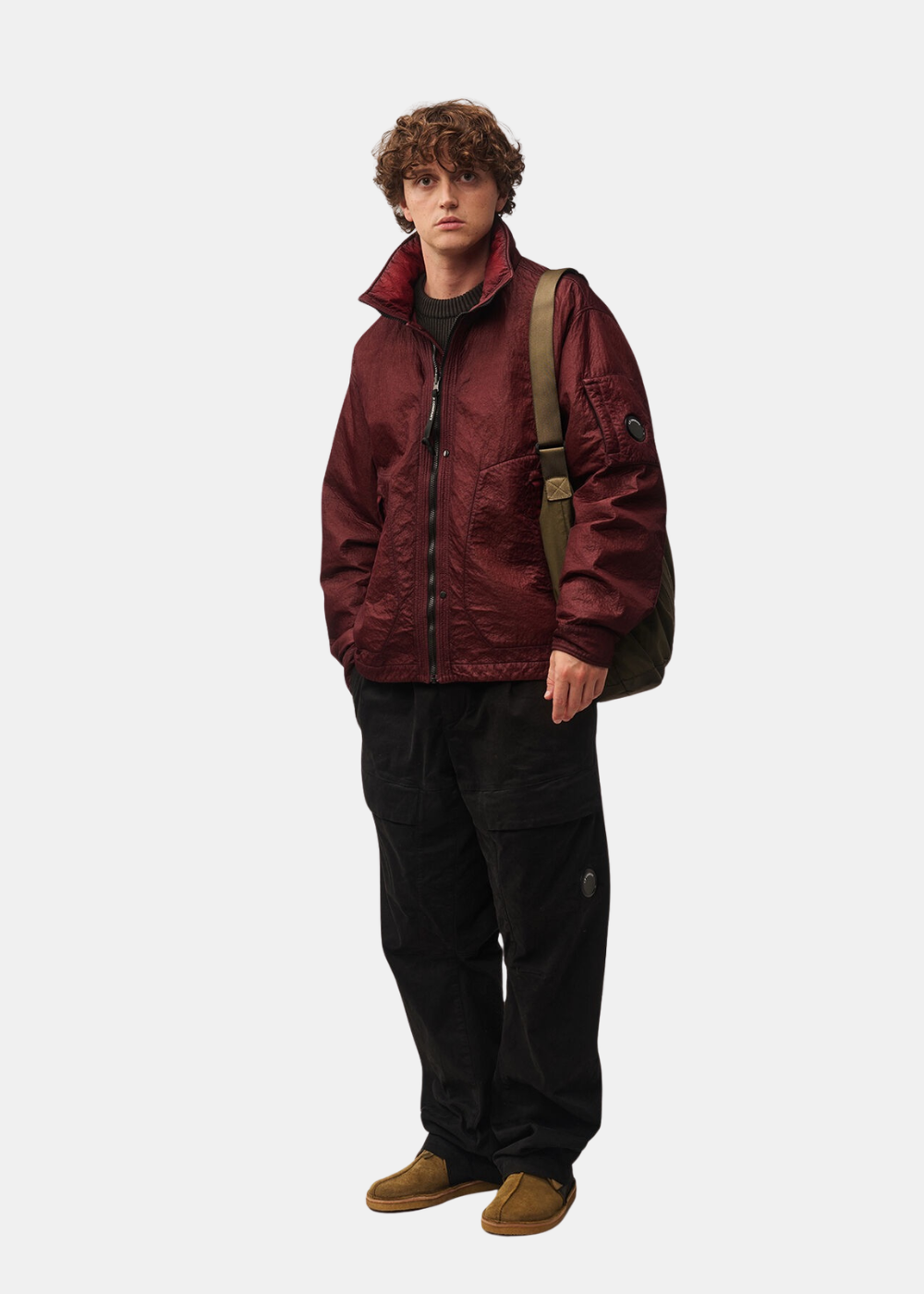 Mannequin homme portant la veste réversible bordeaux C.P. Company avec un pantalon noir, un sac en bandoulière et des chaussures en daim