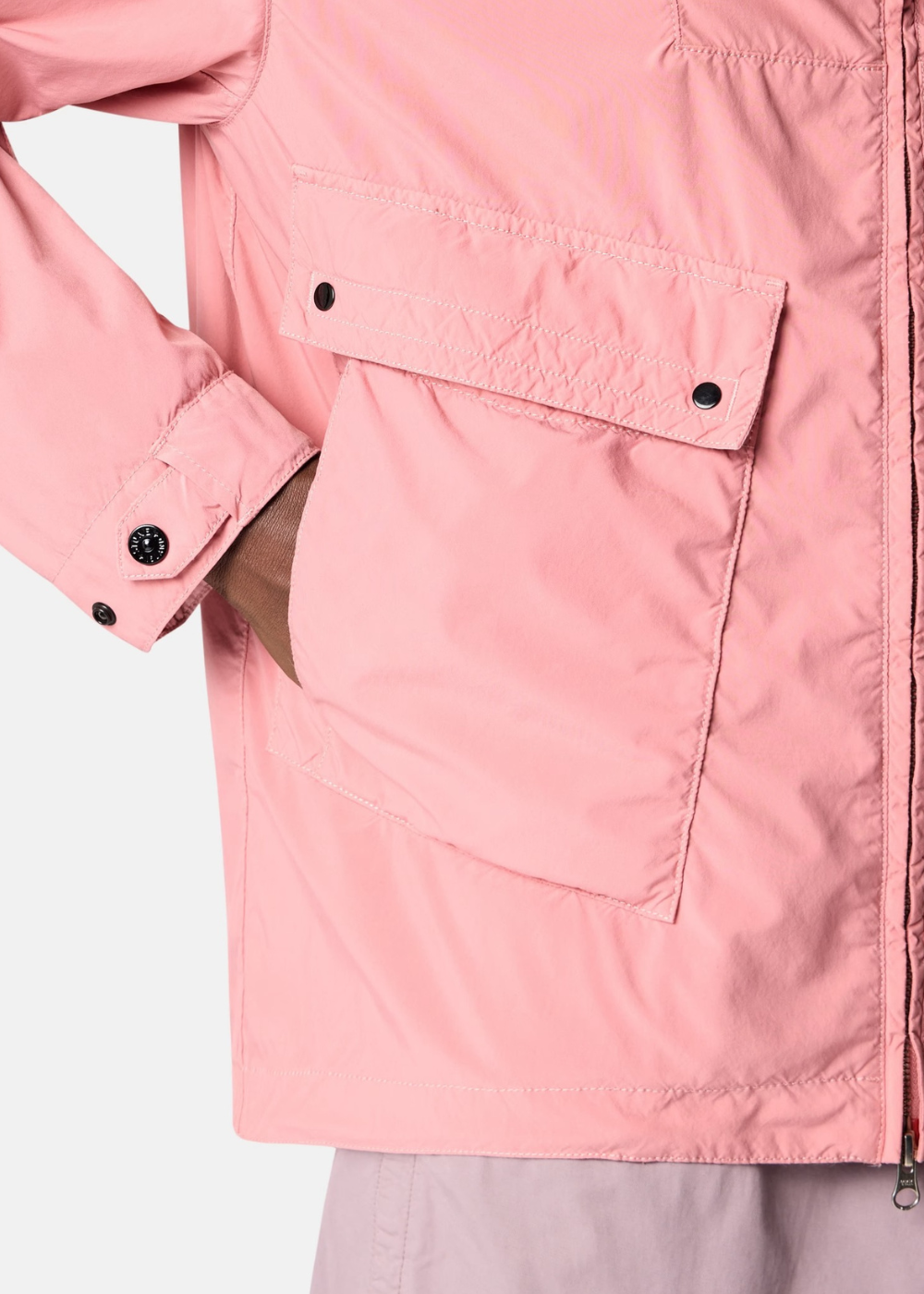 Gros plan sur la poche cargo et le bouton pression d'une veste technique rose Stone Island.