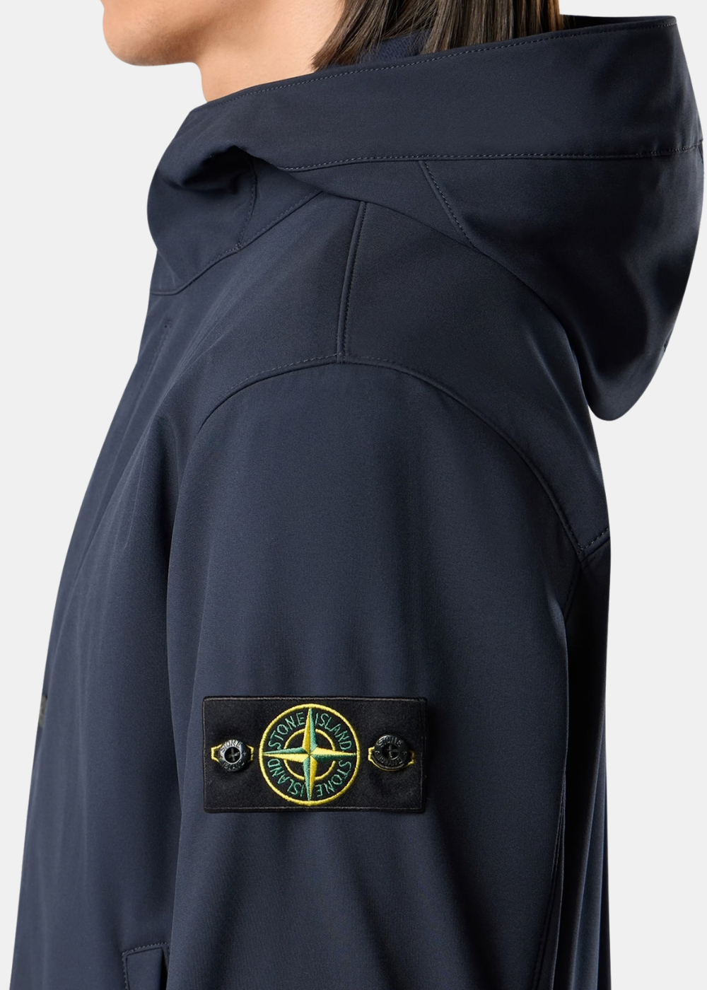 Primer plano del parche con la brújula característico de Stone Island en la manga de la chaqueta azul marino