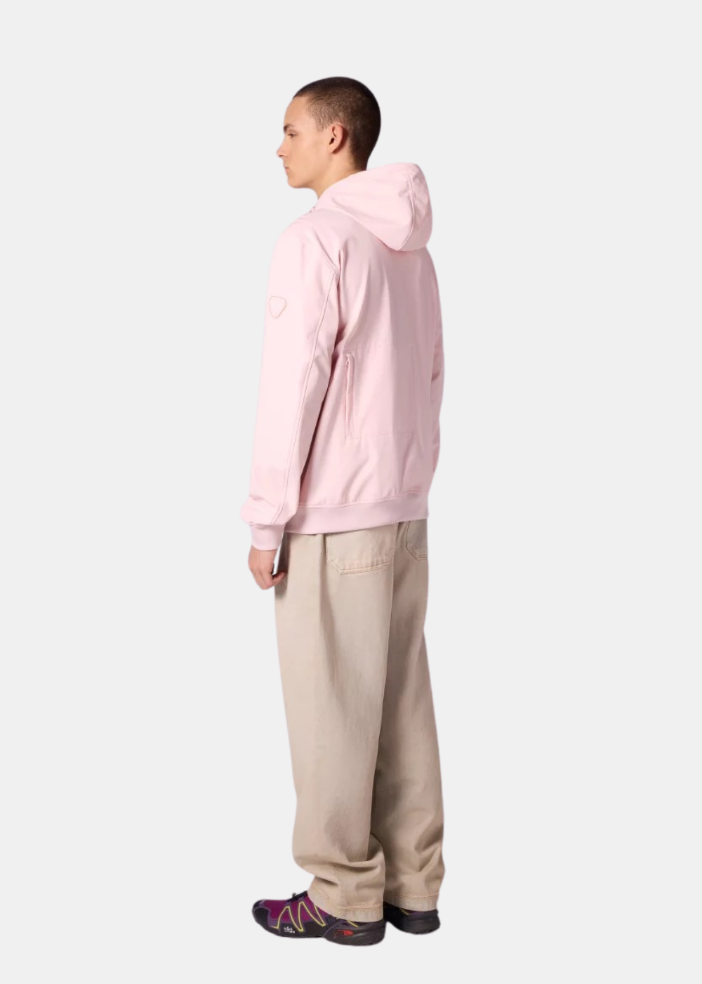 Vue de trois-quart dos d'un homme portant la veste technique Gertrude Ronaldo rose pastel avec un pantalon beige.