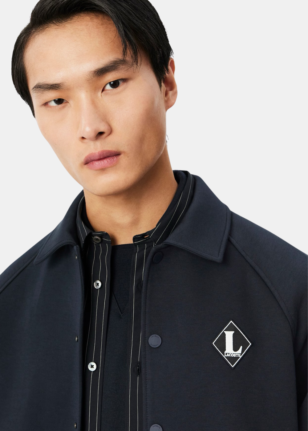 Zoom sur le badge losange rétro L Lacoste en piqué sur la poitrine de la veste marine.