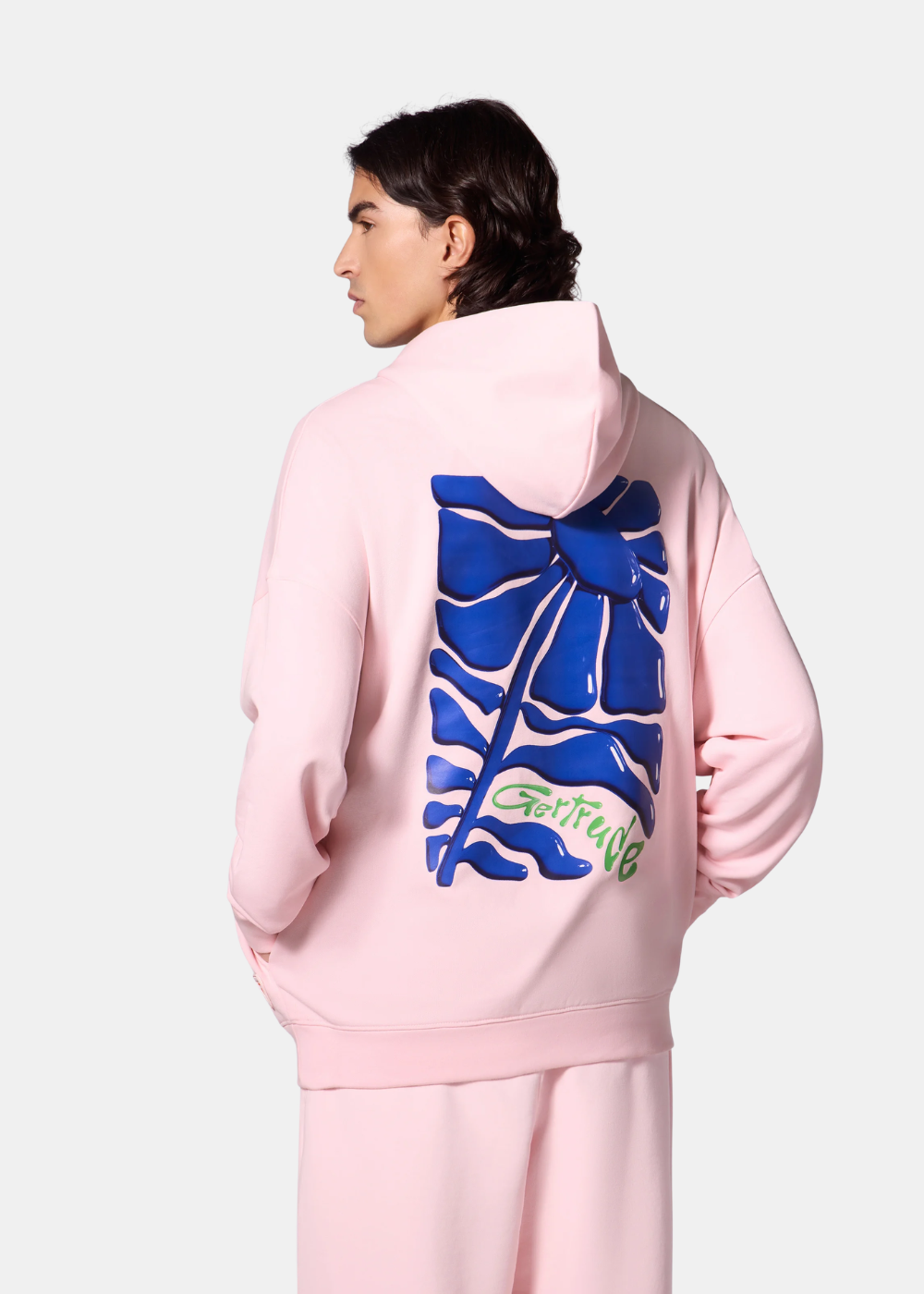 cette photo montre le sweat à capuche Gertrude rose porté par un mannequin. On voit en détail le logo gertrude qui represente une fleur bleu.