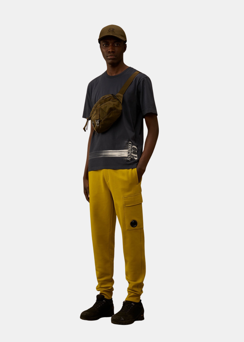 Tenue complète avec t-shirt navy, pantalon jaune, sac bandoulière olive et casquette assortie.